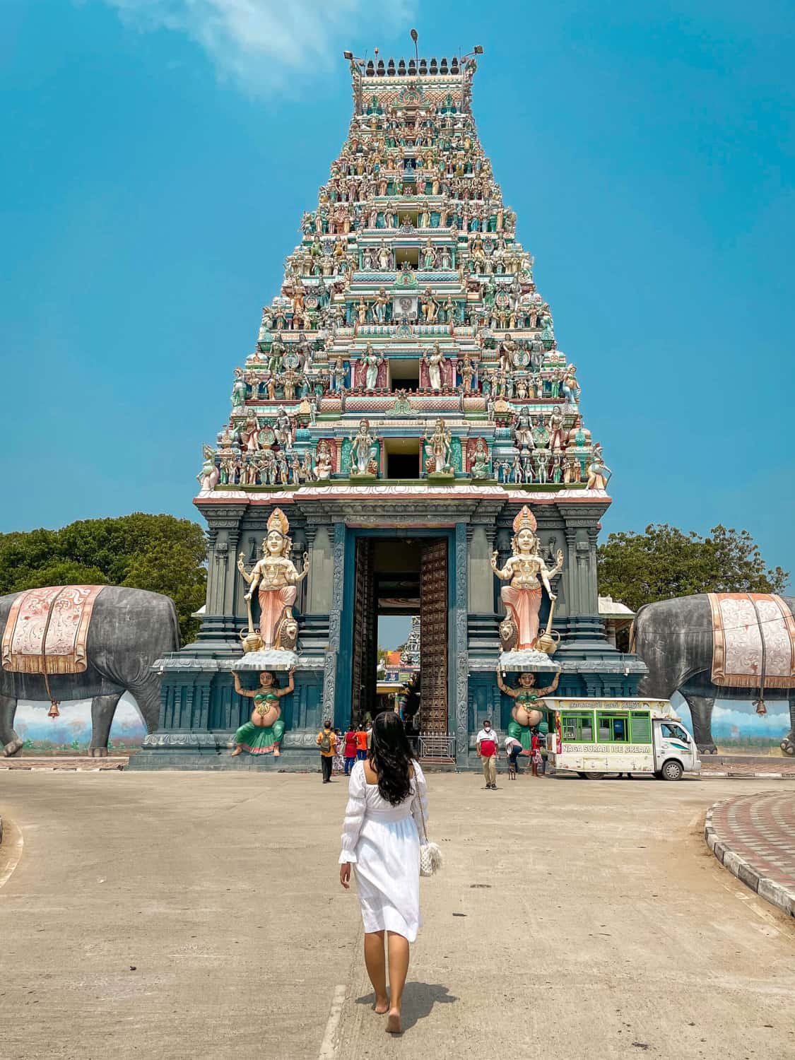A woman in a white dress walks toward a large, ornate Hindu temple entrance adorned with colorful statues of deities and mythical figures in Nainatheevu, Jaffna.