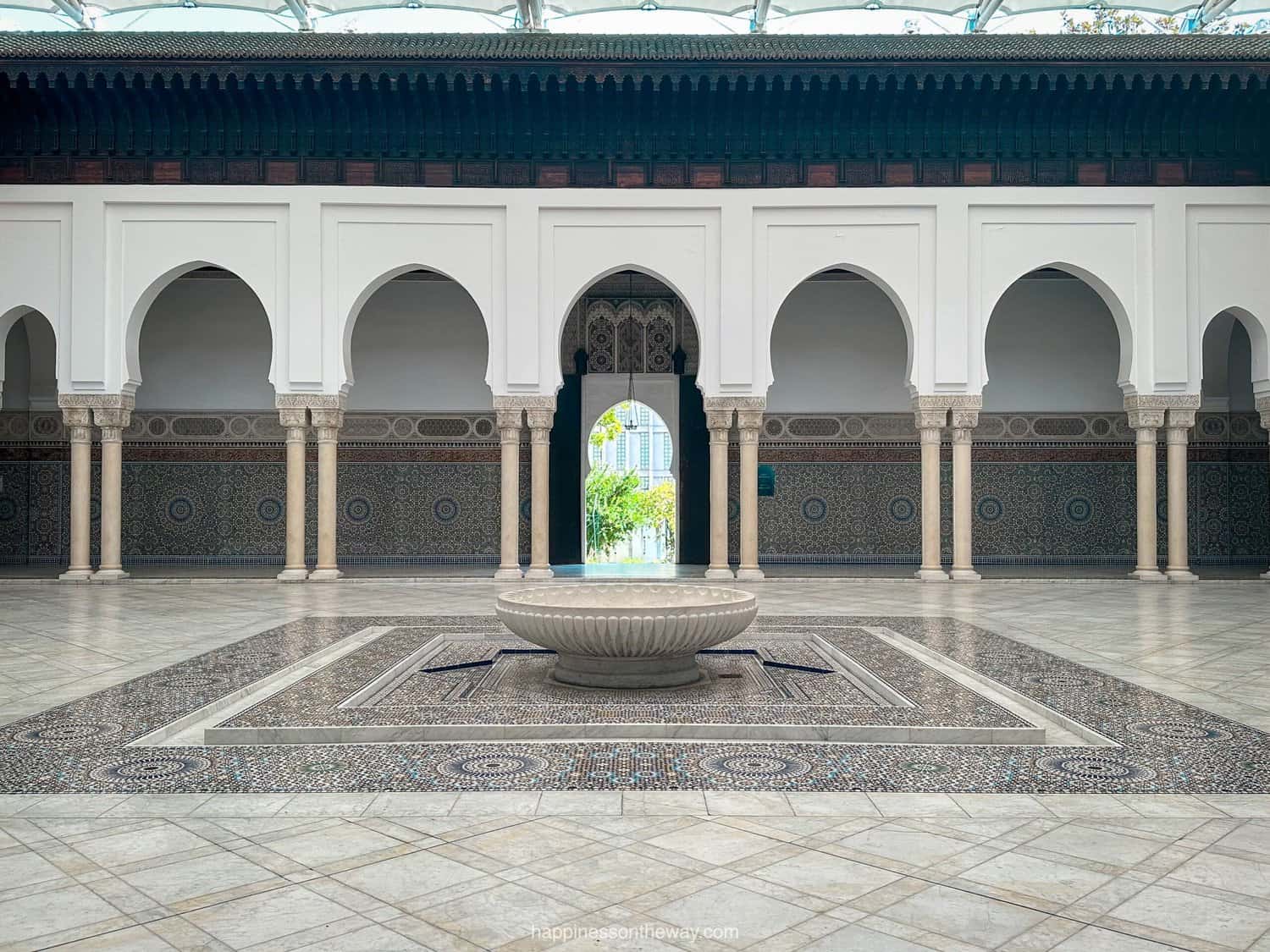 Courtyard of the  Grande Mosque de Paris adorned with colorful geometric-patterned mosaics and lush greenery.