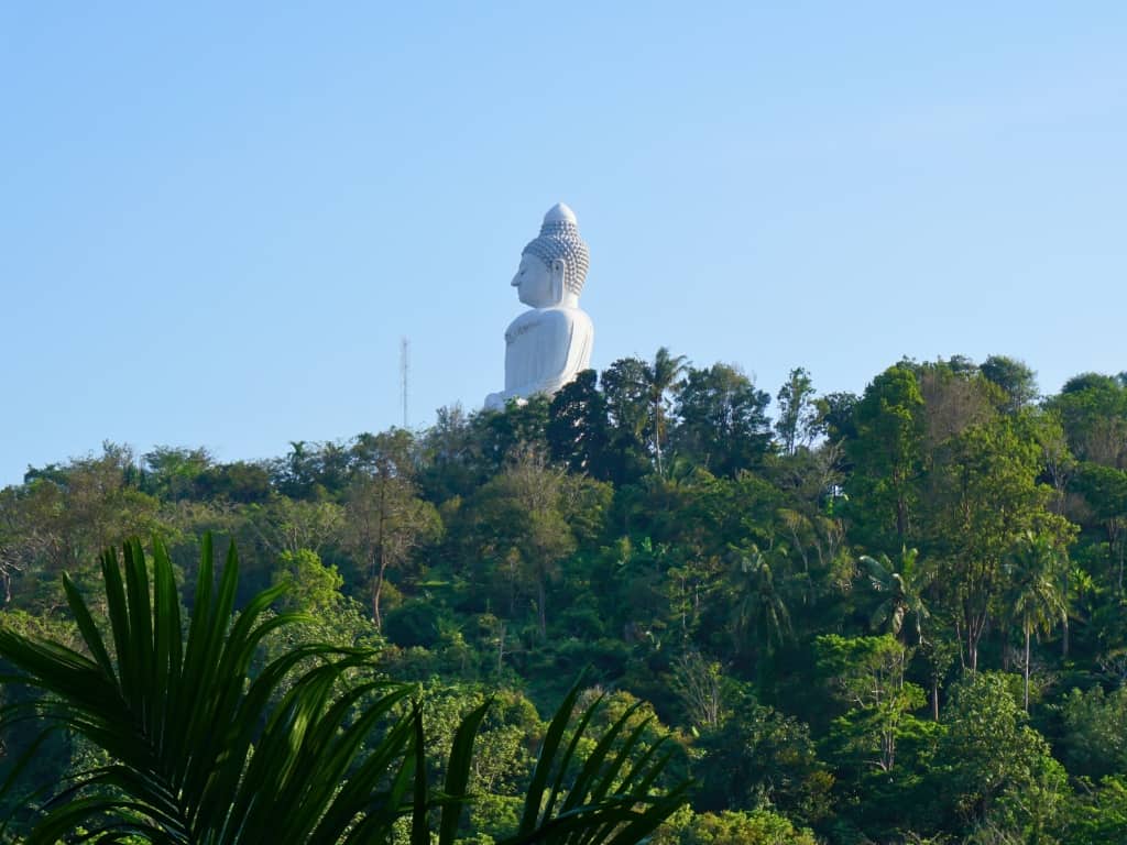 View of the statue of the Big Buddha Phuket against trees that you can see on a view point during a Big Buddha Phuket hike or ATV.