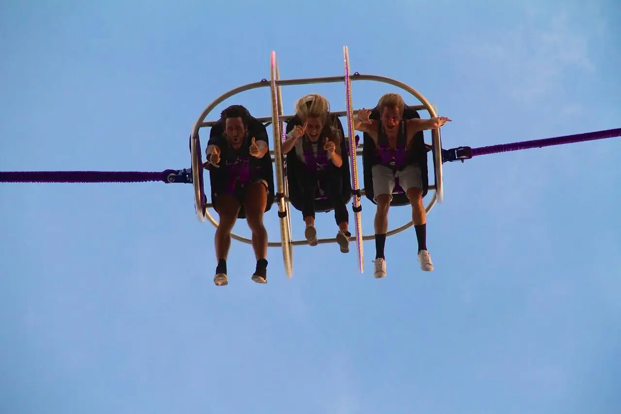 Three individuals strapped into a reverse bungee ride at 5GX Bali, suspended mid-air against a clear blue sky. 