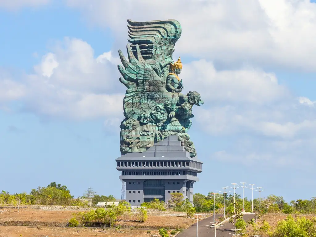 Garuda Wisnu Kencana statue in Bali, Indonesia, standing against a backdrop of blue skies and scattered clouds.