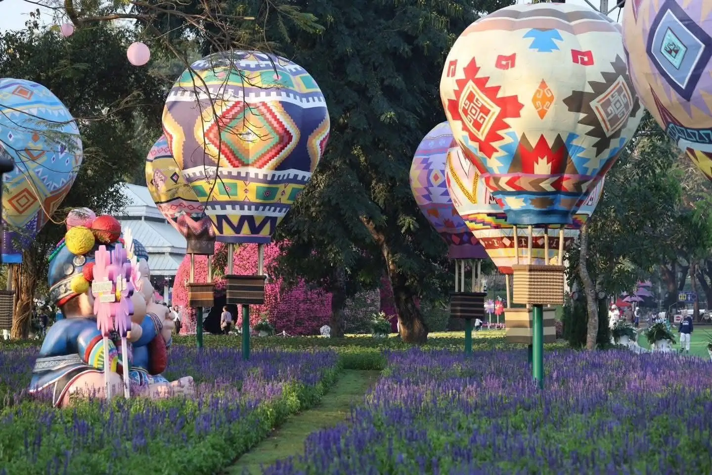 Colorful hot air balloon sculptures rising above purple flower beds at the Chiang Rai Flower Festival in Thailand.