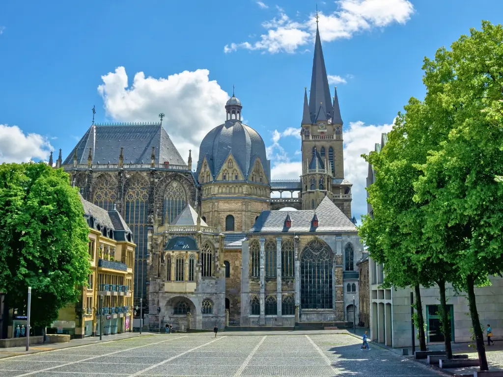 The Aachen Cathedral in Germany, a stunning example of medieval architecture with intricate Gothic details, captured on a sunny day with green trees surrounding the structure, a must-see on the best day trips from Paris by train to other countries.