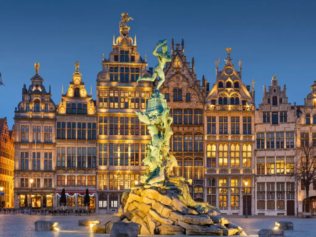 Twilight view of the Grote Markt in Antwerp, Belgium, showcasing the Brabo Fountain and illuminated 16th-century guild houses. Antwerp is among the famous day trips from Paris by train to other countries.