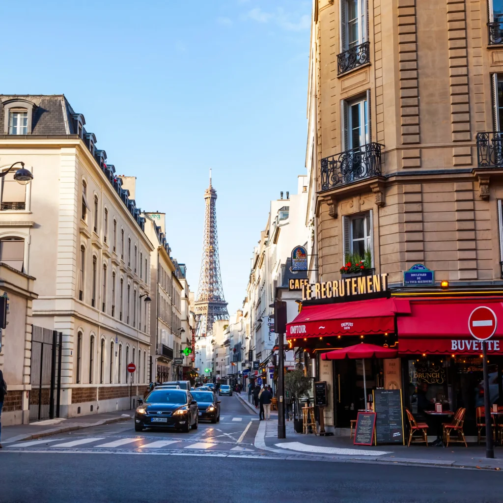 Vibrant street view from Rue Saint-Dominique with the Eiffel Tower in the background, Parisian cafes and bistros lining the sidewalk, and cars and pedestrians adding to the dynamic city atmosphere on a clear day.