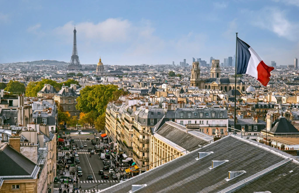A panoramic view Paris with the Eiffel Tower in the distance and the French flag flying prominently in the foreground. This view of Paris is from the top of Pantheon.