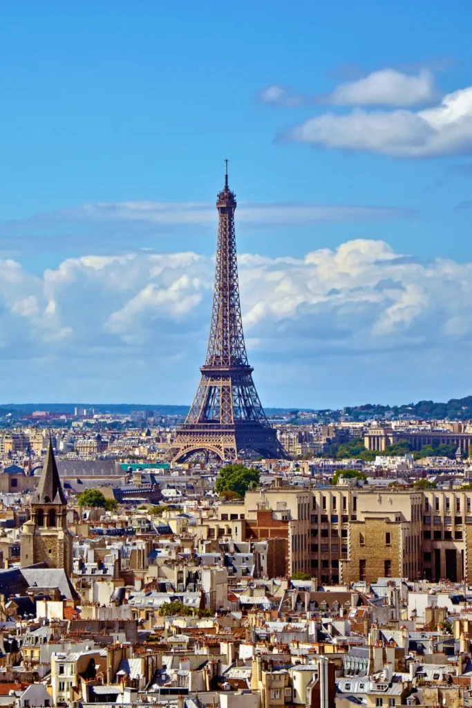 One of the best views of the Eiffel Tower standing tall amidst the Paris skyline, as seen from the viewpoint of Cathédrale Notre-Dame de Paris, with a vibrant blue sky dotted with clouds.