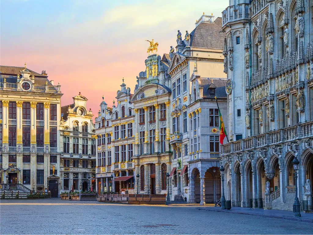 The Grand Place in Brussels at dusk, showcasing the historic guild houses with ornate facades, and the cobblestone square bathed in the warm glow of a setting sun