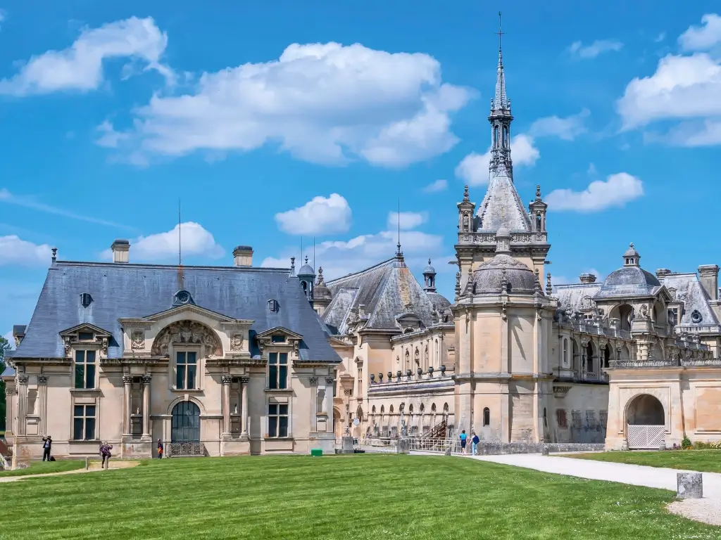 The elegant Château de Chantilly, with its classical French architecture and ornate towers, under a clear blue sky. This historical gem is a highlight among the best day trips from Paris by train, offering a peaceful escape into France's rich heritage.