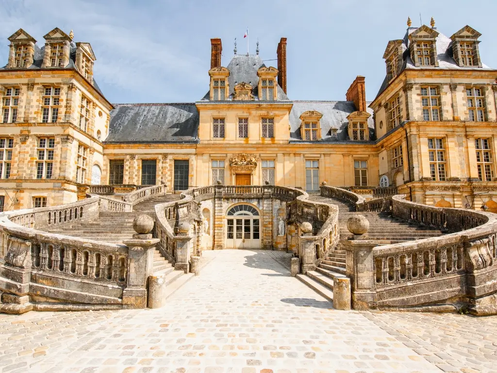 The grand entrance of the Château de Fontainebleau, framed by its majestic horseshoe-shaped staircase, showcases the Renaissance architecture and stately elegance, inviting visitors to explore one of France’s historical treasures. An easy day trip from Paris by train.