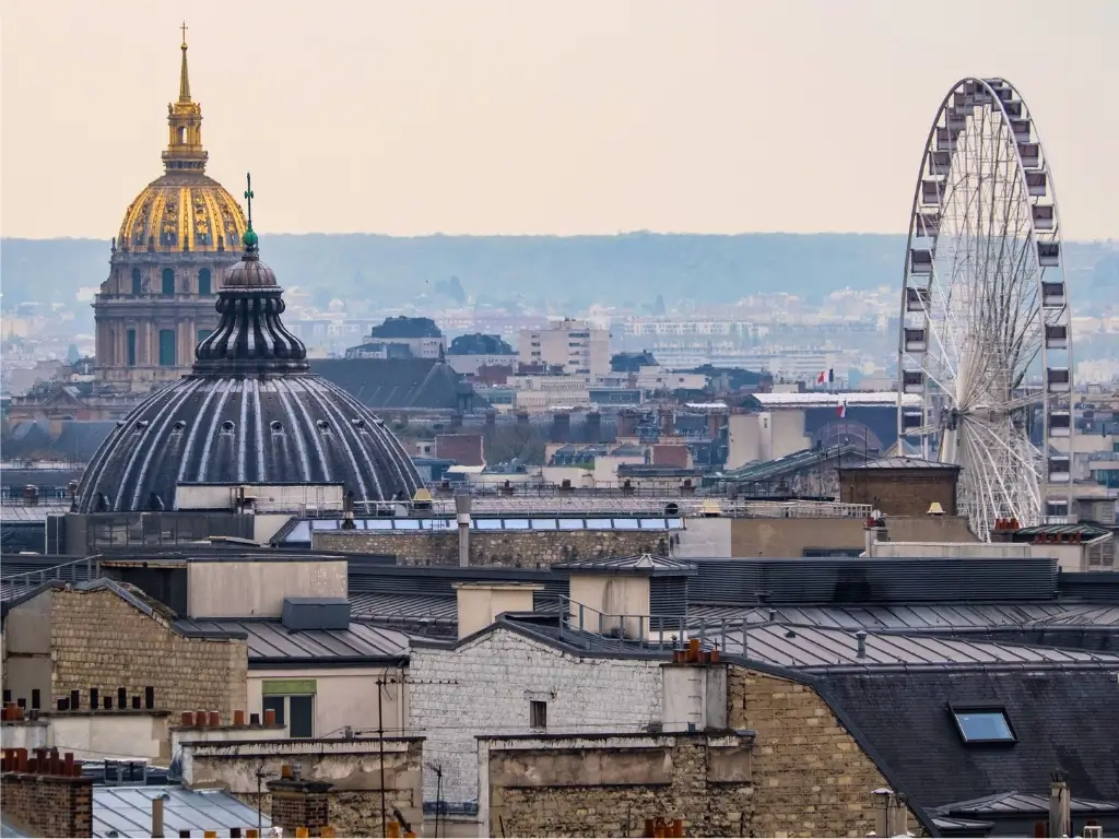 Sweeping view over the Parisian rooftops from the rooftop of Galeries Lafayette. It highlights the city's signature zinc roofs and terracotta chimney pots, under a clear blue sky — a prime spot for free panoramic views of Paris.