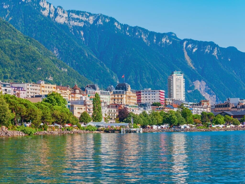View of Geneva, Switzerland, with vibrant buildings lining the lake's edge and the majestic Alps in the background, a popular destination for the best day trips from Paris by train to other countries.