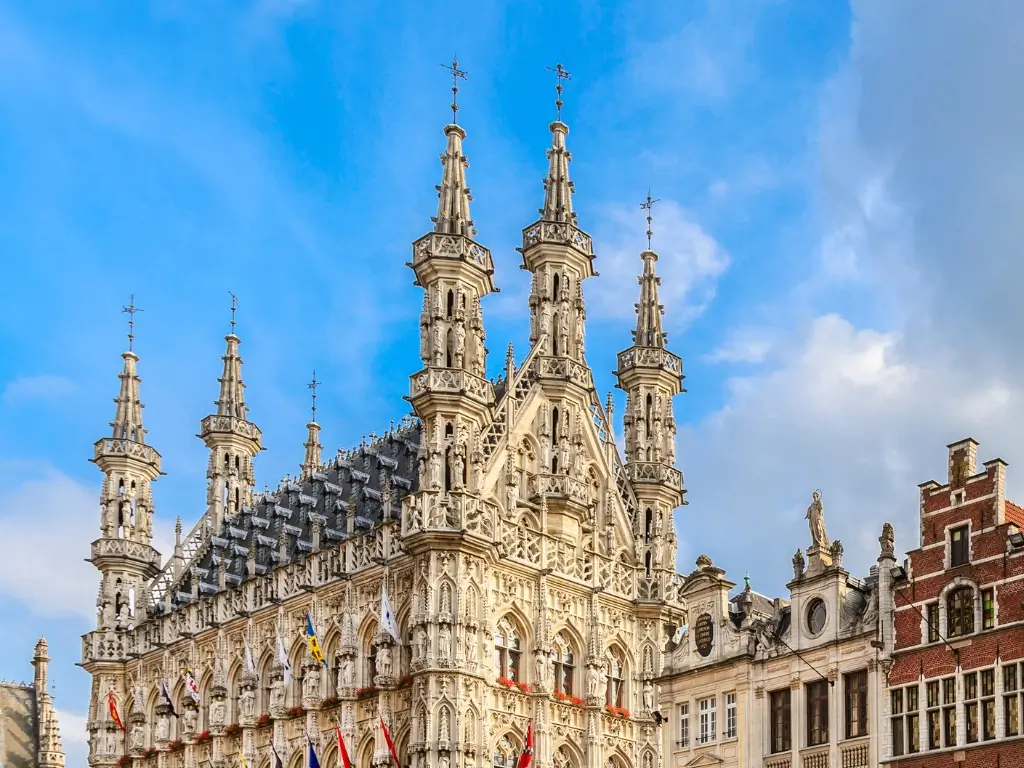 The ornate Gothic architecture of the Leuven Town Hall in Belgium, with its numerous statues and spires reaching into the blue sky, perfectly encapsulates the architectural treasures to be discovered on the best day trips from Paris by train to other countries.