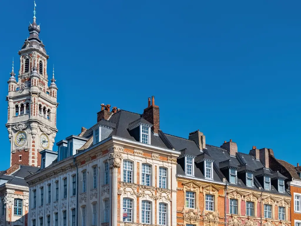 The striking Belfry of the Chamber of Commerce in Lille, France, towers above the classic French and Flemish Renaissance-style buildings, under a clear blue sky. This cultural and architectural richness is what makes Lille a top destination for the best day trips from Paris by train.