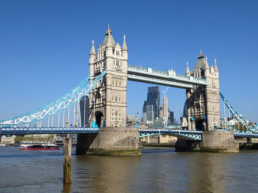 View of the iconic Tower Bridge in London under a clear blue sky, with a red sightseeing boat on the Thames River, often visited during the best day trips from Paris by train to other countries.