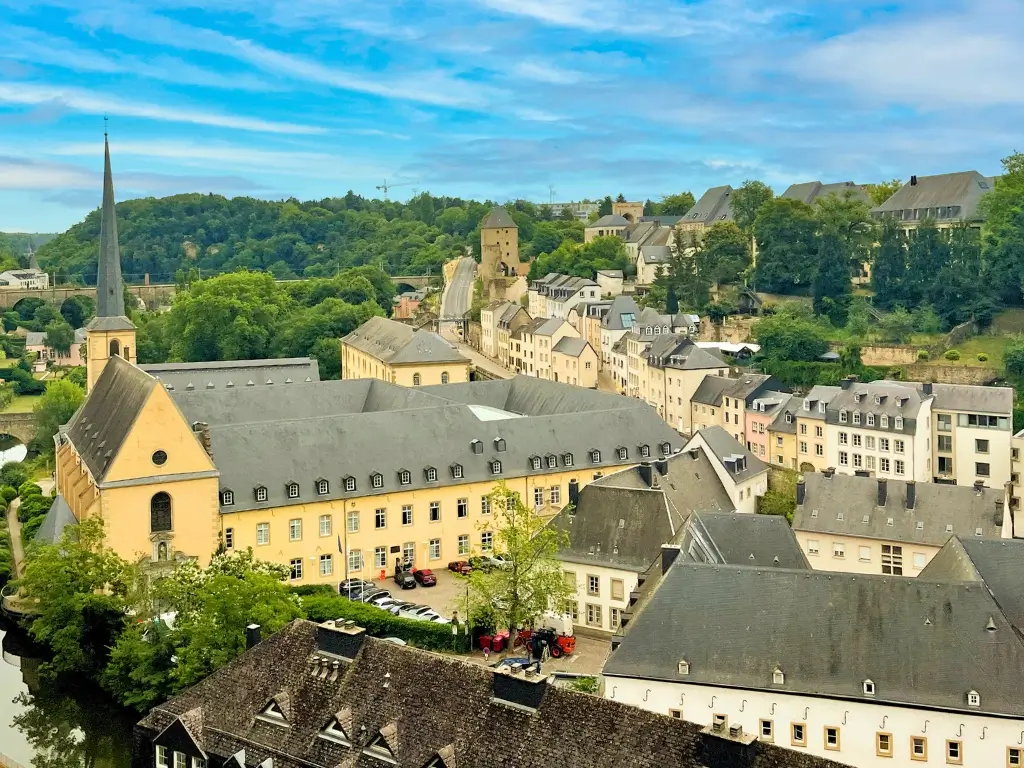Aerial view of Luxembourg City's historic architecture with a spire church, terraced buildings, and tree-covered hills. Luxembourg is one of the best day trips from Paris by train to other countries.