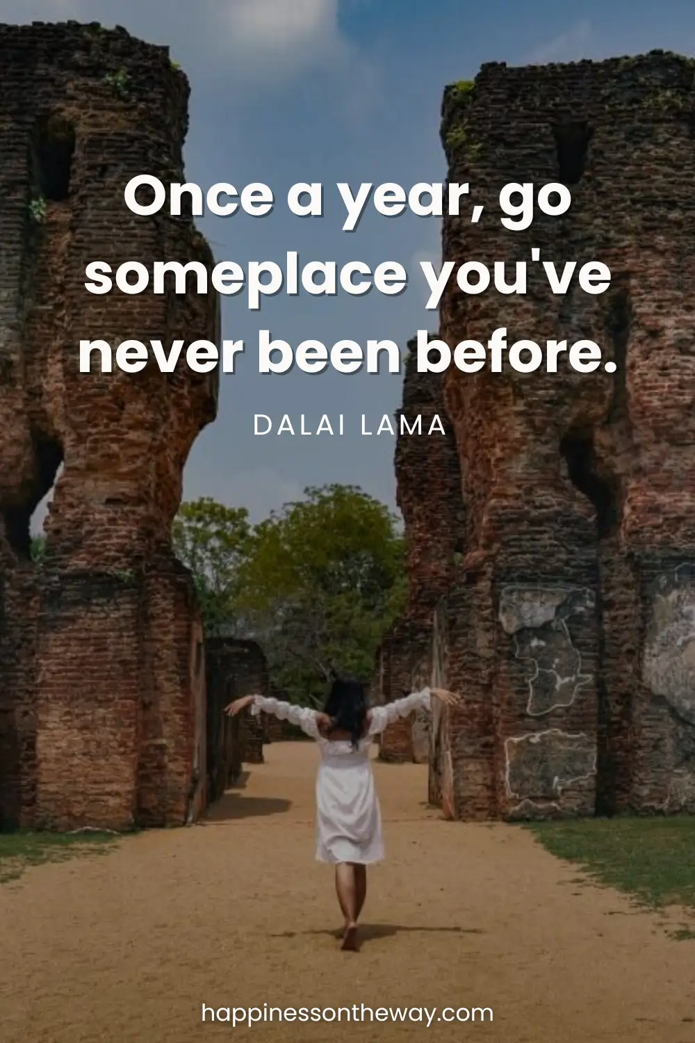Me with outstretched arms in a white dress standing between ancient stone ruins under a clear sky, with the Dalai Lama quote 'Once a year, go someplace you've never been before.'
