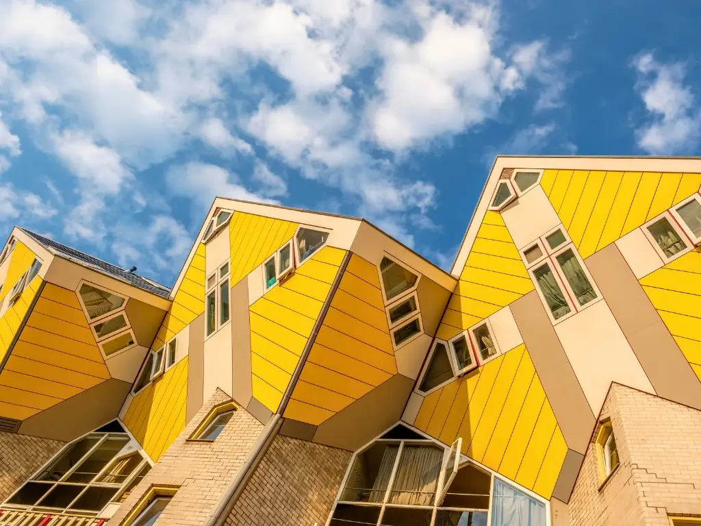 Unique cube houses in Rotterdam, Netherlands, with their yellow facades and unconventional tilted design against a blue sky with fluffy clouds, embodying the innovative architecture that awaits on the best day trips from Paris by train to other countries.