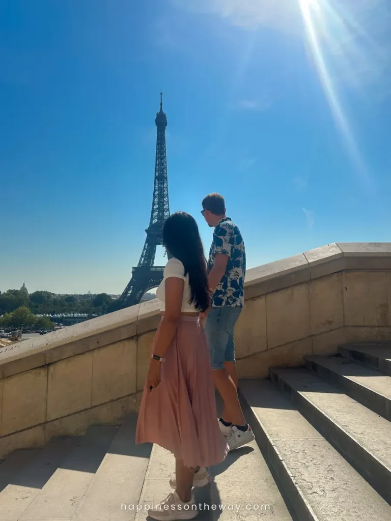 Us standing on the steps of Trocadéro, with the best views of Eiffel Tower in the background and the sun casting a soft glare, creating a romantic scene in one of the best free views in Paris