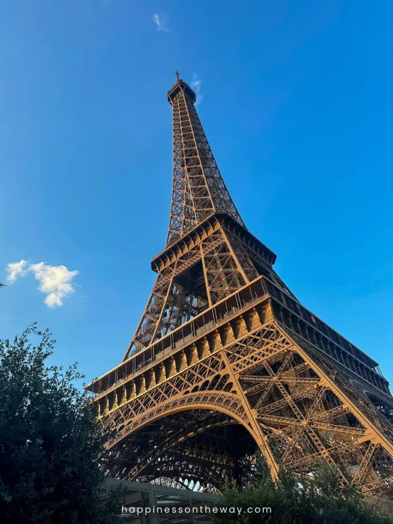The imposing structure of the Eiffel Tower viewed from directly underneath, showcasing the intricate iron lattice work against a backdrop of a clear blue sky.