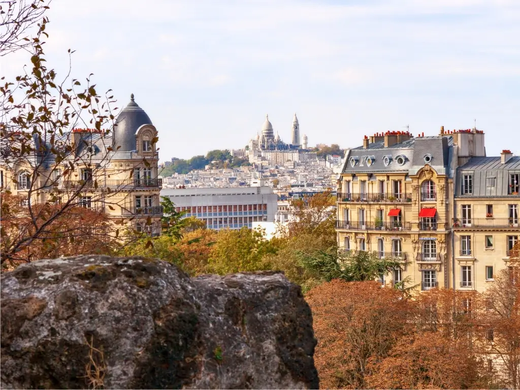 One of the best Paris viewpoints featuring the iconic Sacré-Cœur Basilica seen from Parc des Buttes-Chaumont, surrounded by classic Parisian architecture and autumn foliage.