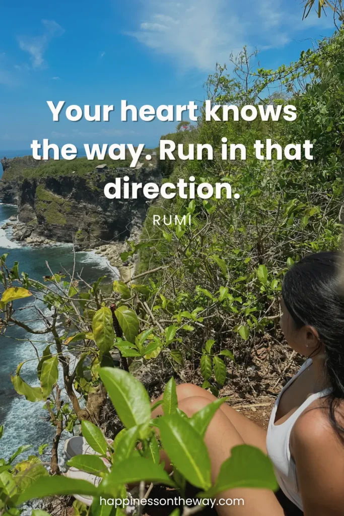 Me in a white tank top looking out over a rugged coastline with lush greenery and blue sea, with the Rumi quote 'Your heart knows the way. Run in that direction.' and the website credit happinessontheway.com at the bottom.