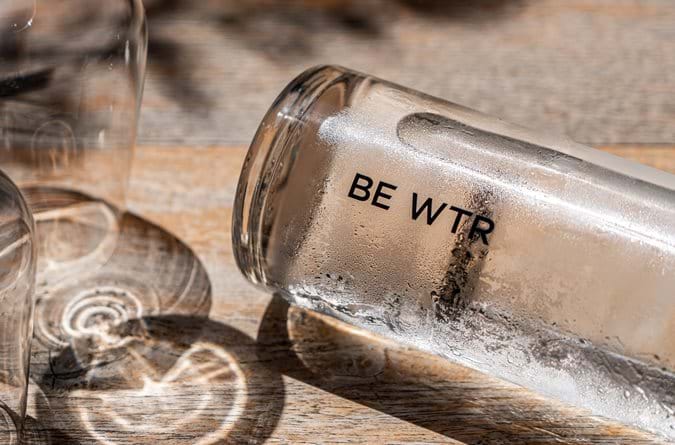 Close-up of a BE WTR glass water bottle tipped over, emphasizing Le Bristol Paris' dedication to sustainability and plastic-free luxury.