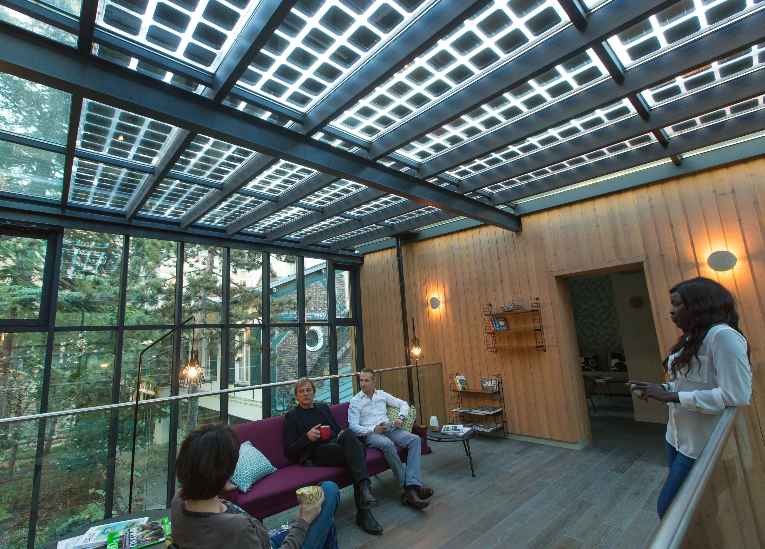 Eden Lodge Paris offers a sustainable meeting room experience under a solar panel glass ceiling, surrounded by wooden interiors and lush greenery, emphasizing eco-friendly business travel.