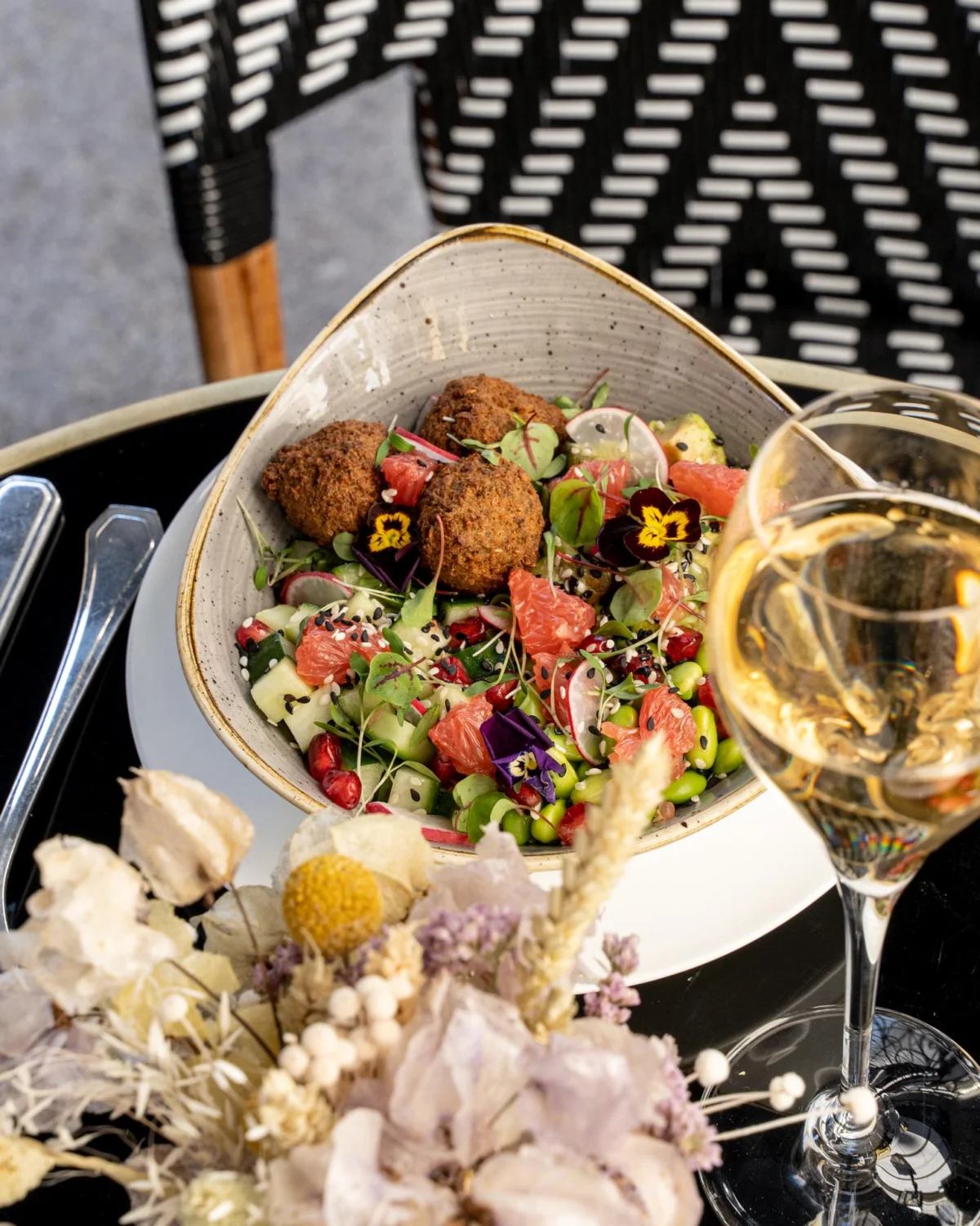 Gourmet salad with vibrant edible flowers and falafel paired with a glass of white wine at Grand Powers Paris, highlighting the hotel's commitment to seasonal and fresh food offerings.