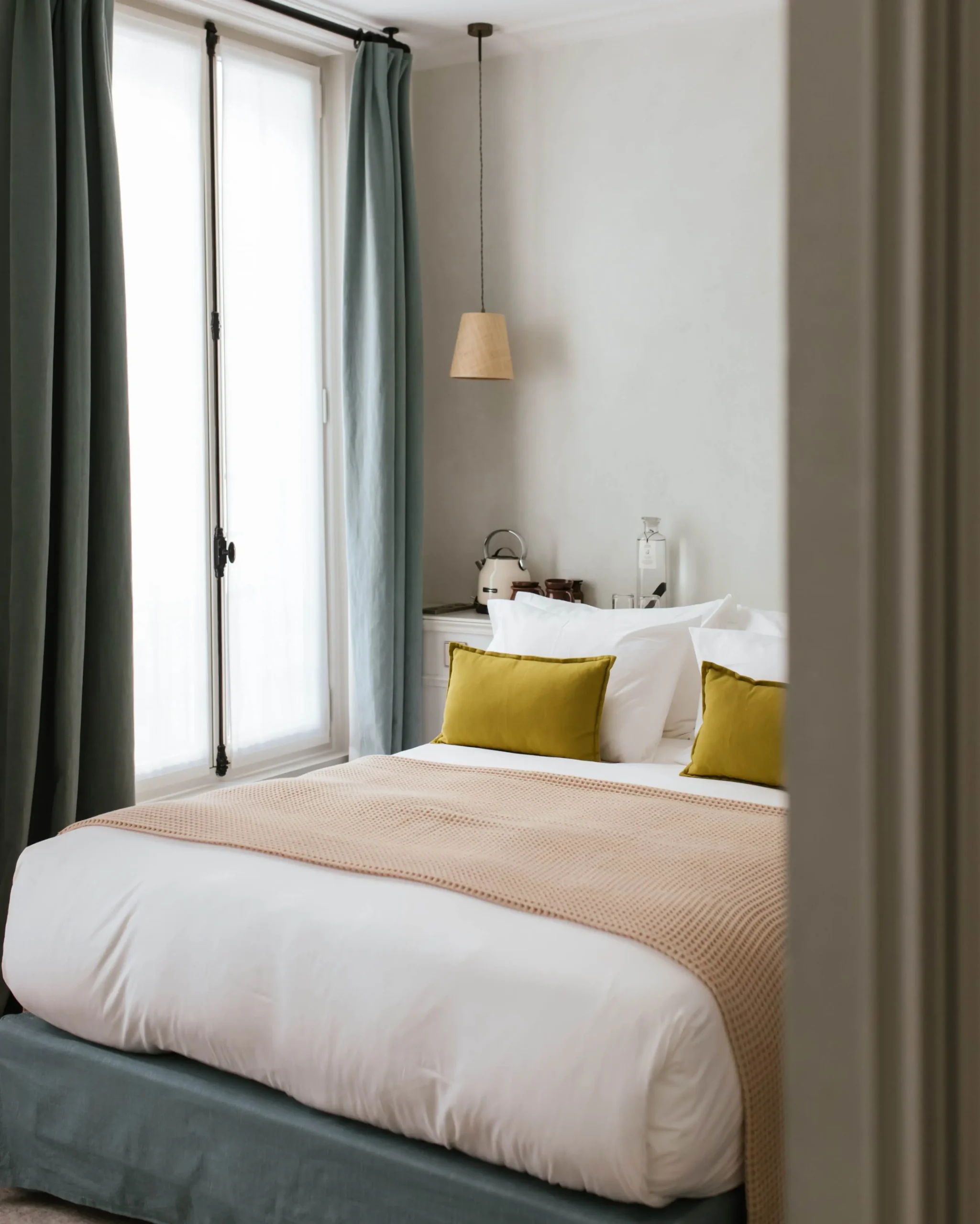 Minimalist yet cozy room at HOY Hotel Paris, reflecting an eco-friendly approach with natural light, crisp linens, and a calm color palette accented by a green headboard and vibrant plants.