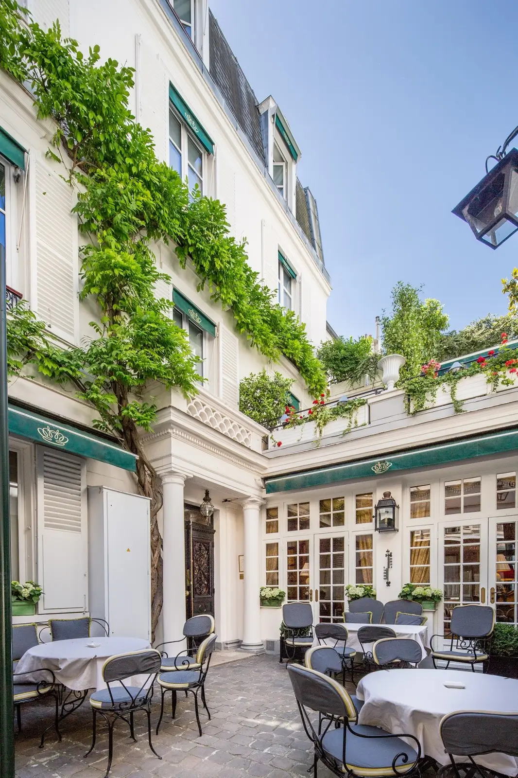 Quaint courtyard at Hotel Duc de Saint Simon in Paris, showcasing a sustainable hotel environment with ivy-clad walls, wrought iron furniture, and potted plants.