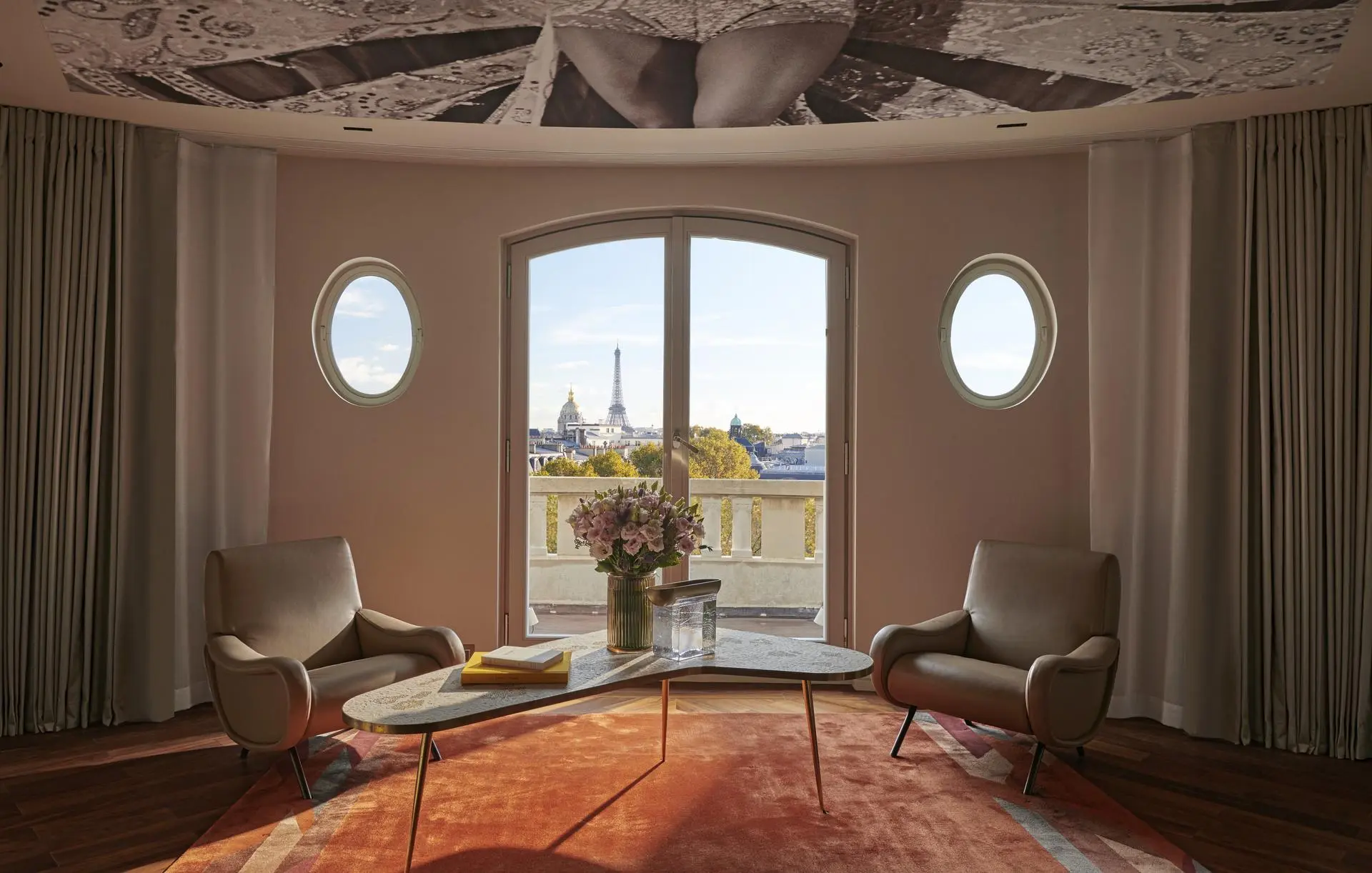 Sophisticated lounge area at Hotel Lutetia, an eco-friendly hotel in Paris, with modern armchairs and a coffee table set against the backdrop of panoramic windows offering a breathtaking view of the Eiffel Tower and Paris skyline.