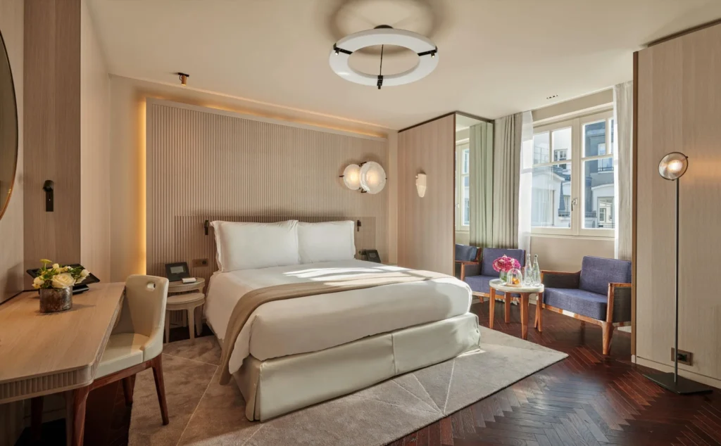 Warm and inviting guest room at Hotel Lutetia, an eco-friendly hotel in Paris, with sleek wood finishes, a plush bed with cream linens, and a cozy sitting area by the window, blending modern design with comfort.