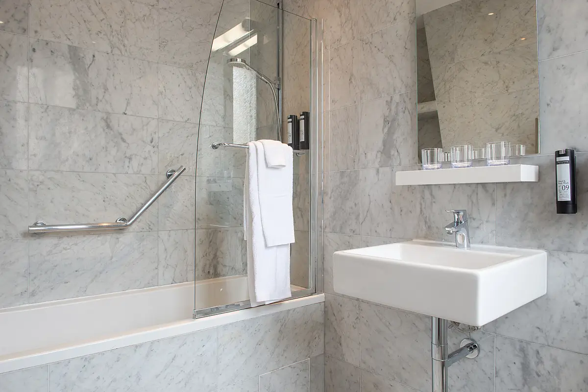Sleek and eco-friendly bathroom at Hôtel de la Porte Dorée in Paris, featuring marble tiling, a modern square basin, and environmentally conscious toiletries.