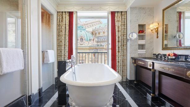 Elegant bathroom with opulent marble accents and a standalone bathtub at InterContinental Paris Le Grand, providing a view of the Parisian architecture through draped windows, for a lavish bath experience.