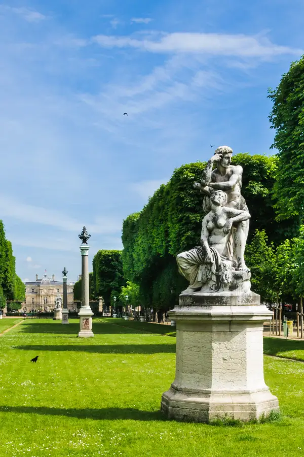 An elegant marble statue dominates the Jardin des Grands Explorateurs, among the best picnic spots in Paris. Surrounded by neatly trimmed hedges and lush lawns, set against a backdrop of stately Parisian buildings and clear skies.