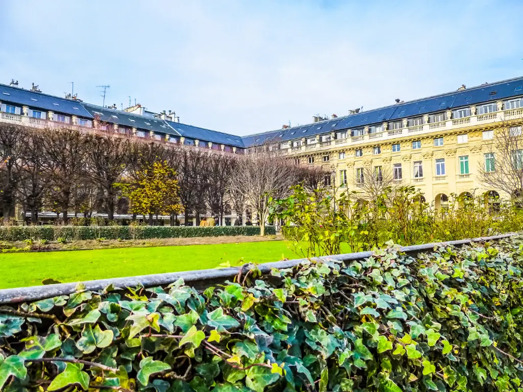 Vibrant Jardin du Palais Royal, a picnic place in Paris, captured on a sunny day, showcasing manicured lawns and hedgerows, with classical Parisian buildings in the background, the garden's symmetry inviting a leisurely stroll.