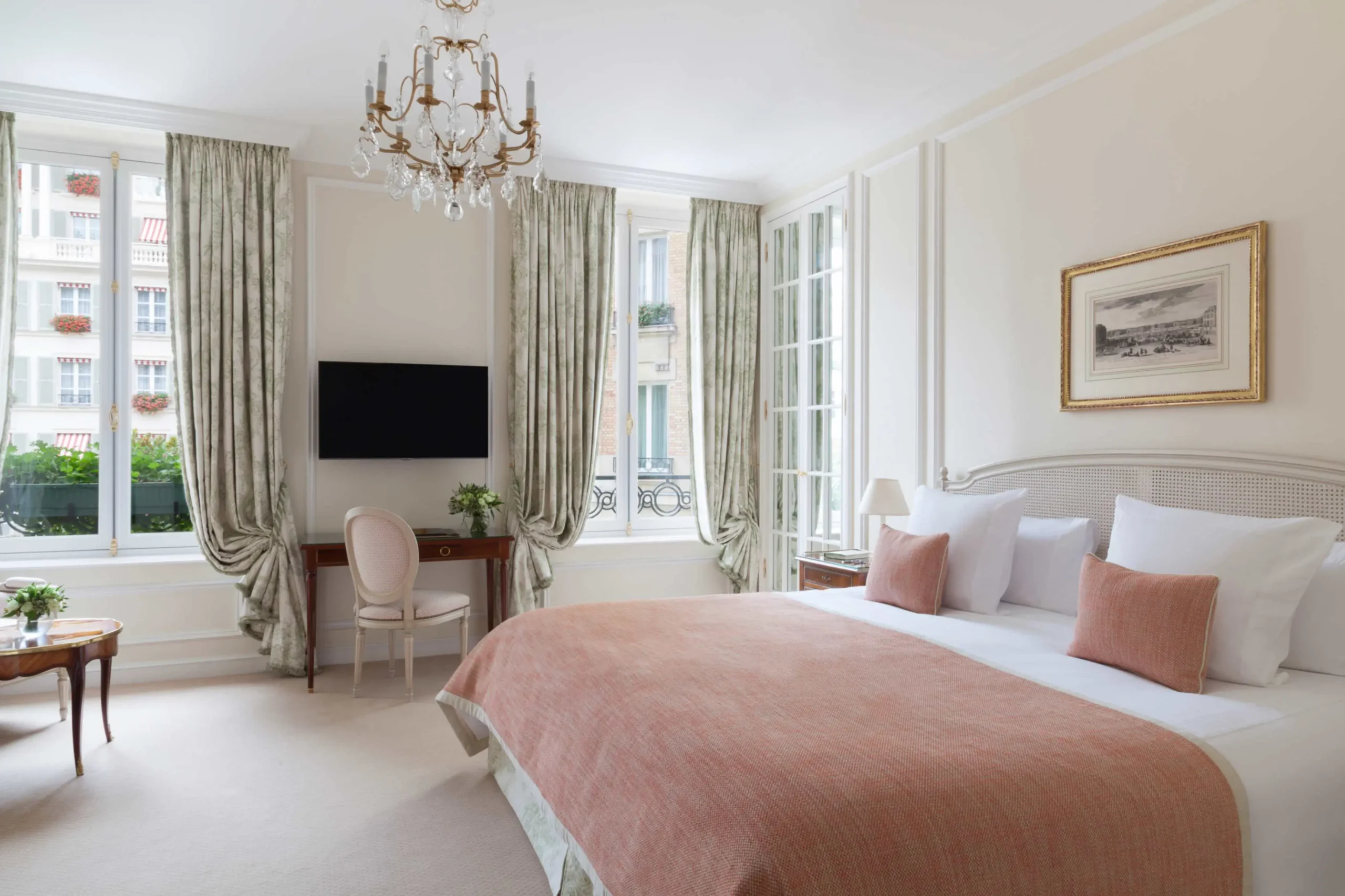 Elegant guest room at Le Bristol Paris, an eco-friendly hotel in Paris, featuring a deluxe-sized bed with crisp blush linens, classic French windows that open to a lush view, and a crystal chandelier adding a touch of luxury.