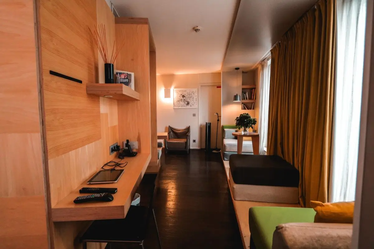 Contemporary living space at Le Citizen Hotel in Paris, featuring a sleek wooden workspace, comfortable seating, and warm yellow drapes, embodying a sustainable and stylish ambiance.