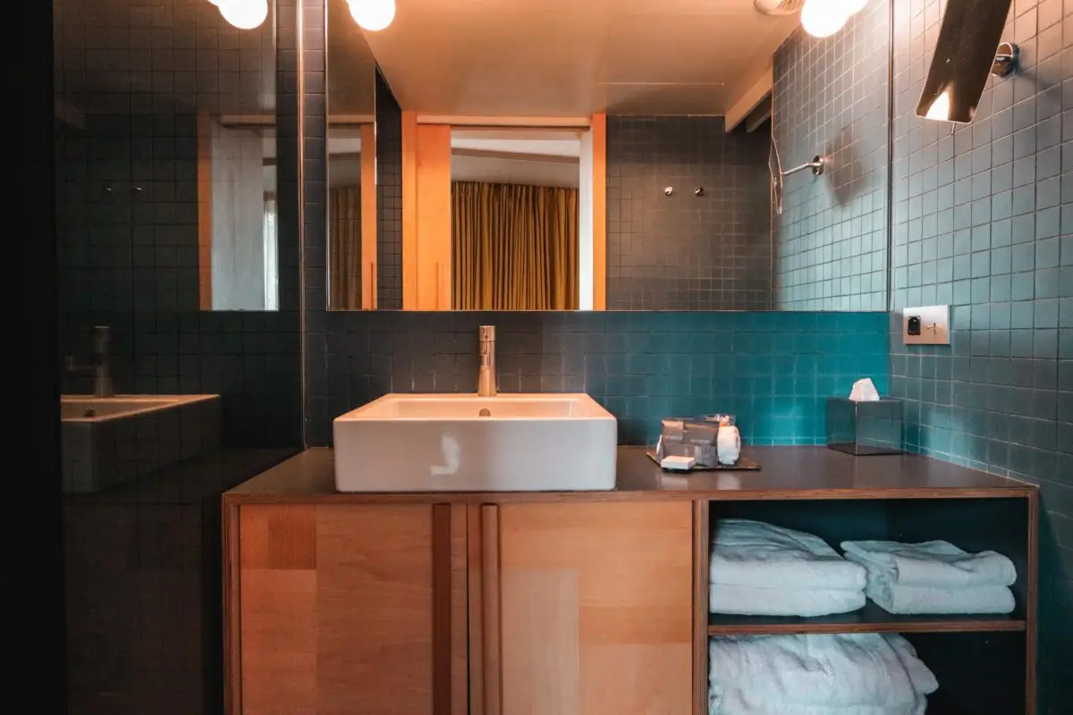 Chic and sustainable bathroom design at Le Citizen Hotel, Paris, with dark teal tiles, a spacious white basin, and wooden accents, reflecting the hotel's commitment to eco-luxury.