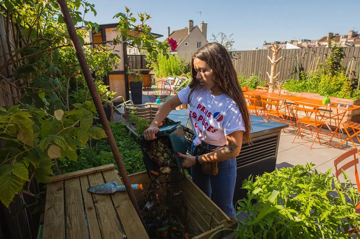 A guest participates in sustainable practices at Mob Hotel in Paris by composting kitchen scraps, with a rooftop garden background, illustrating the hotel's commitment to eco-friendly initiatives.