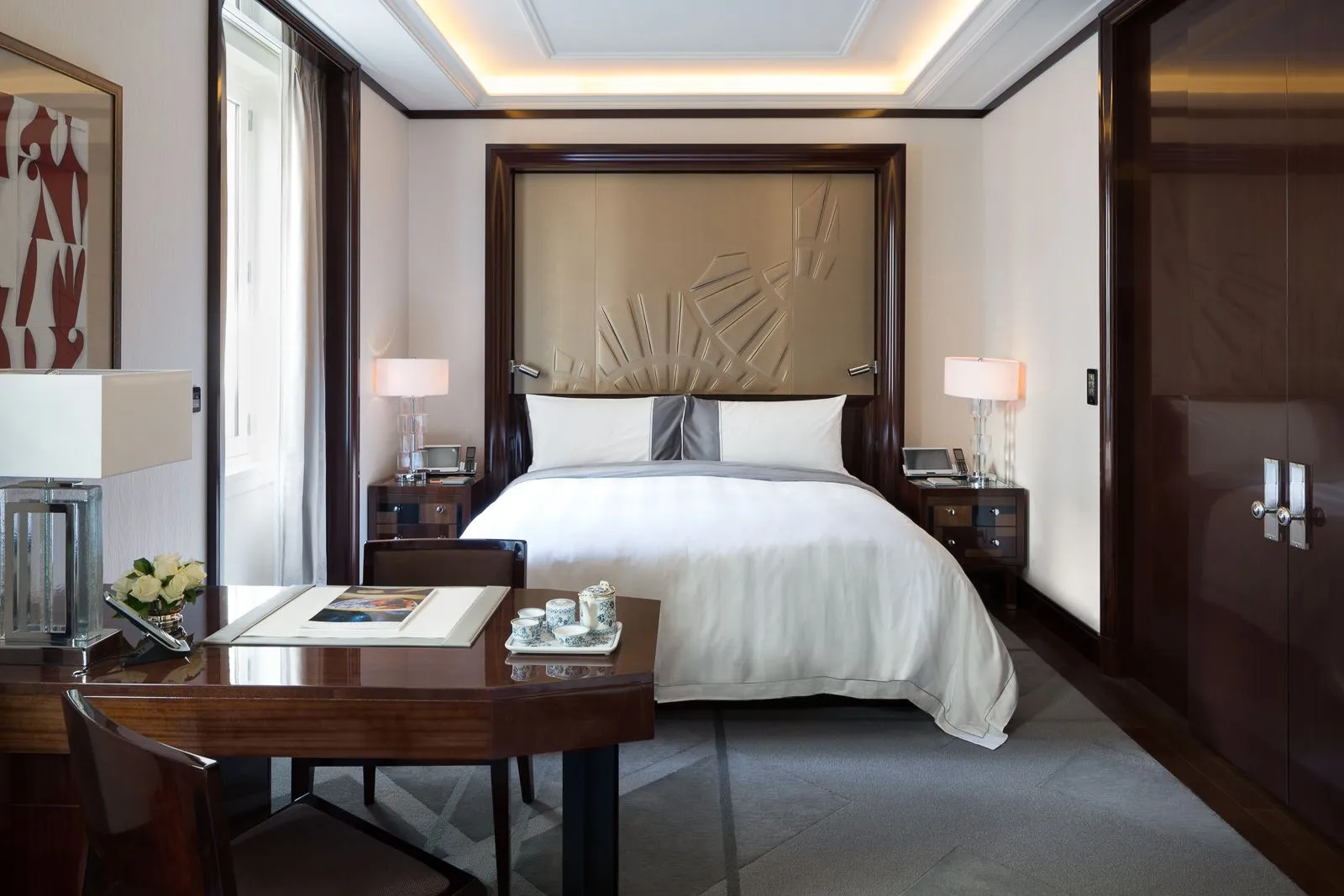 A refined and sustainable bedroom at Peninsula Paris, displaying a luxurious bed with crisp linens, a sleek work desk with traditional tea service, and warm ambient lighting, capturing the essence of eco-friendly elegance.