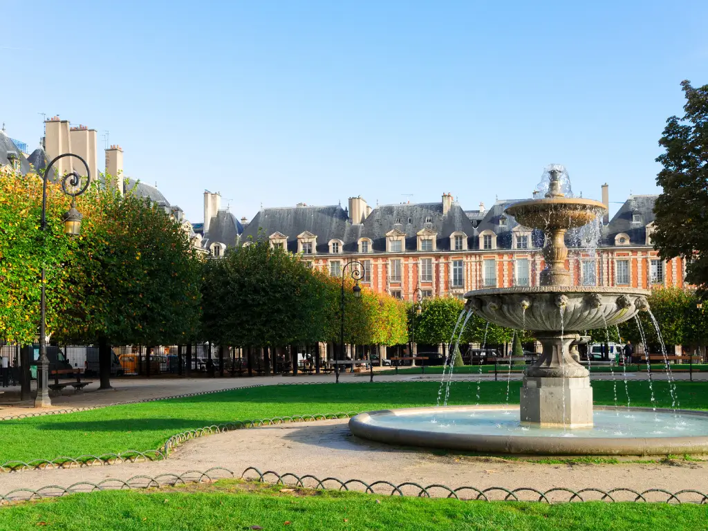 Place des Vosges, a picnic place in Paris, showcasing its distinctive red-brick buildings and symmetrically placed trees, with a central fountain gently cascading water, embodying classical French elegance.