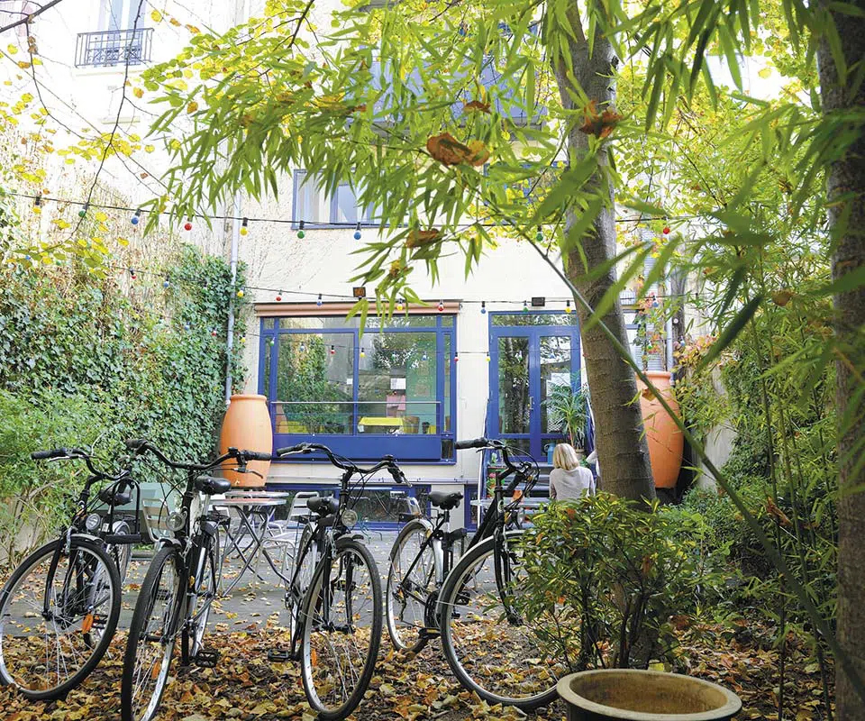 Eco-conscious Solar Hotel in Paris provides free bicycles for guests, parked in a leafy courtyard with views of the hotel's colorful facade.