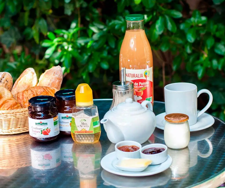 Sustainable breakfast at Solar Hotel Paris with fresh bread, organic jams, honey, and apple juice set on a table surrounded by greenery, showcasing the hotel's commitment to eco-friendly practices.