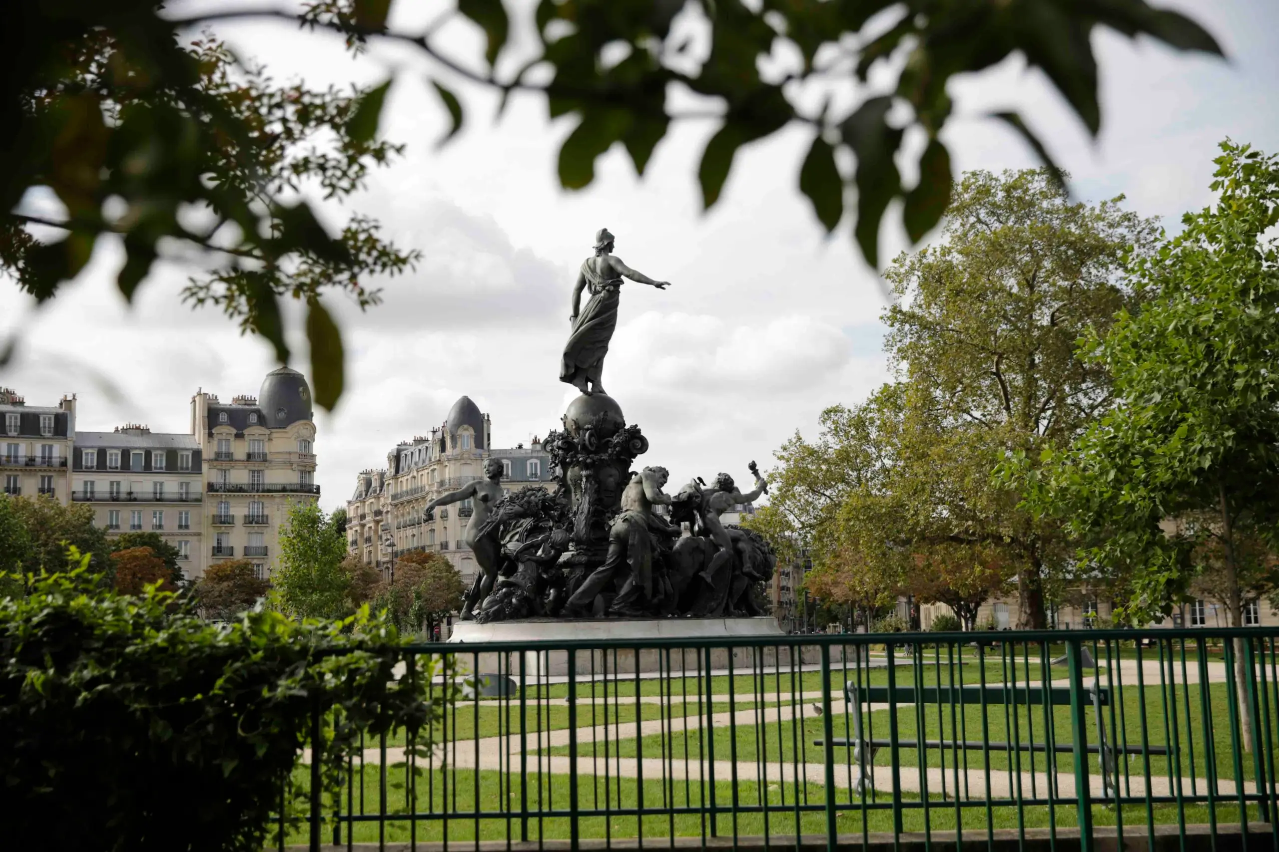 Statue of La Place de la Nation peeks through foliage, framed by Parisian architecture and a foreground of greenery, near The People Paris Nation hostel.