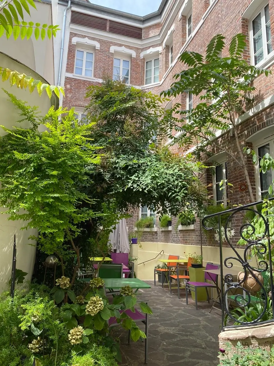 A tranquil garden space at Hotel Pavillon Paris, showcasing eco-friendly outdoor seating amidst vibrant greenery and blooming flowers for a serene urban retreat.
