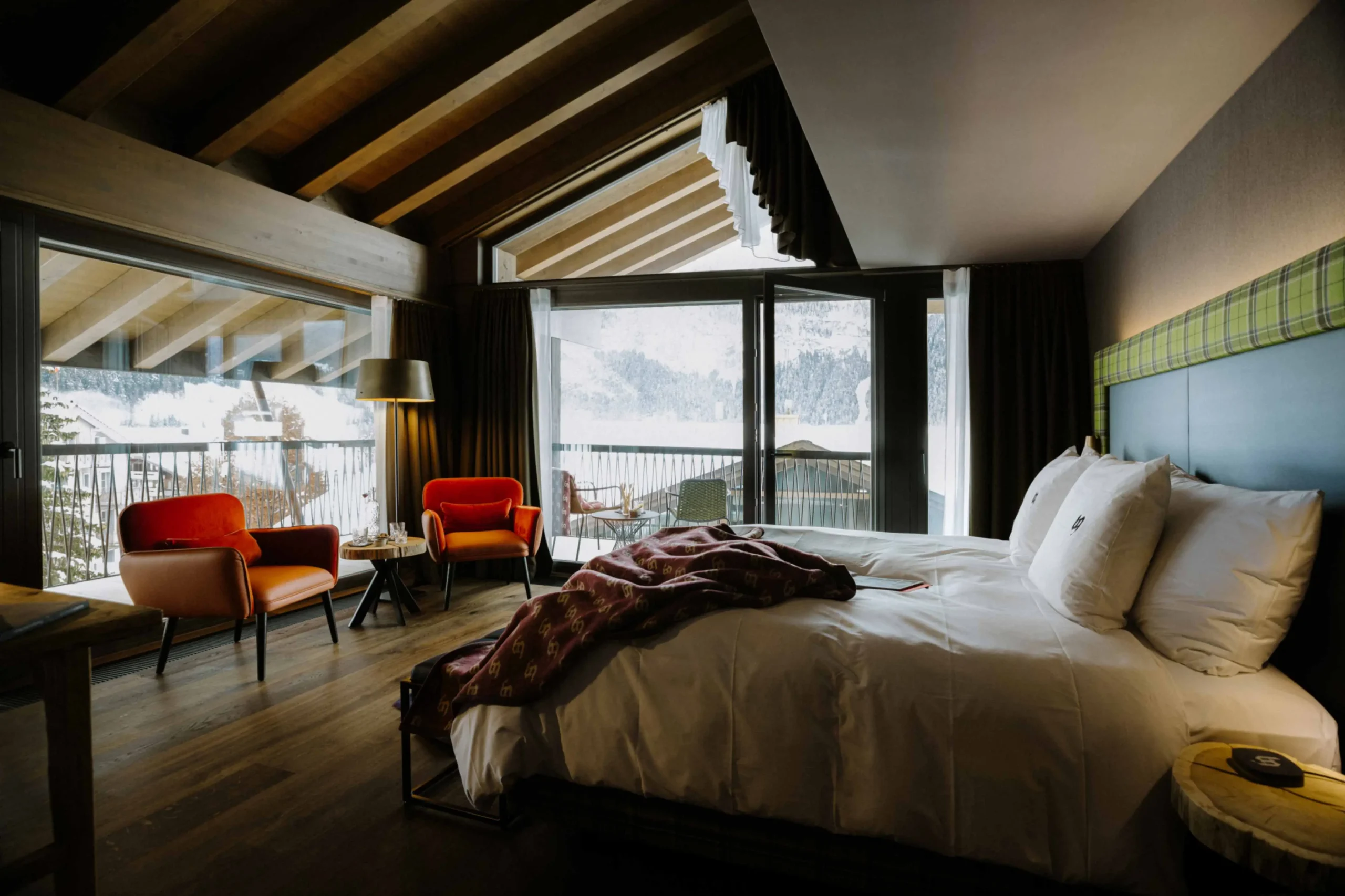 A modern and stylish room of Bergwelt Grindelwald Alpine Design with a plush bed, elegant wooden accents, and expansive windows that open up to a stunning view of the snowy Grindelwald mountains, blending luxury with alpine charm.