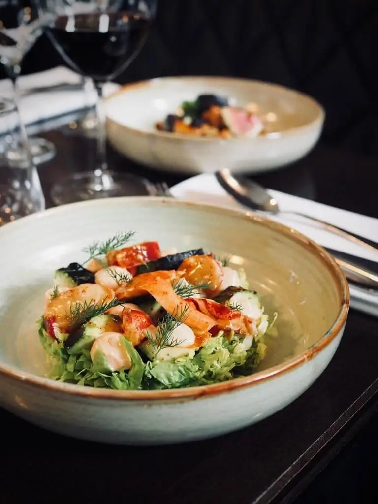 Close-up of a fresh seafood salad at Bistrot Marloe in Paris, served in a ceramic bowl with a glass of red wine in the background.