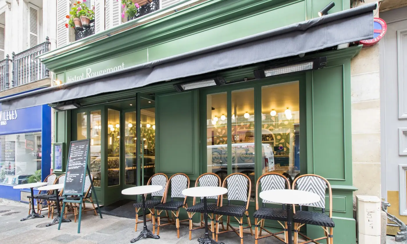 Exterior view of Bistrot Rougemont in Paris with its green facade, outdoor bistro chairs, and a chalkboard menu inviting patrons into the warm atmosphere.